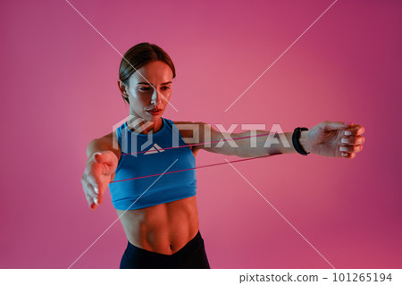 Strong woman in sportswear performs fitness exercises with resistance band on studio background 101265194