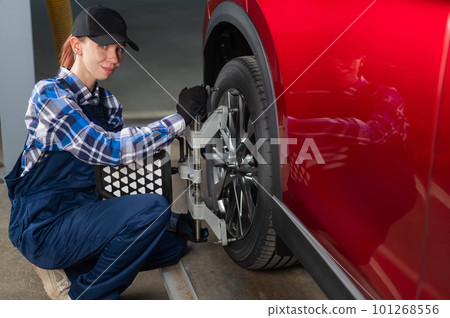 A female auto mechanic makes a camber. Woman working in a car service. 101268556