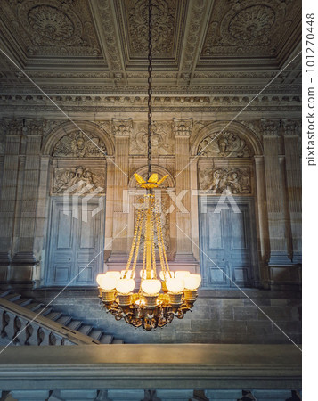 Architectural details of a staircase, ornate hall and glowing vintage chandelier hangs from ceiling, Versailles Palace, France. 101270448