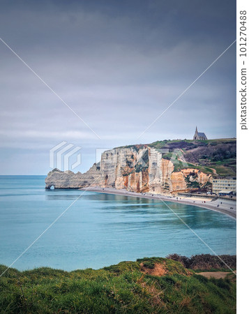 Idyllic view to Etretat coastline with the famous Notre-Dame de la Garde chapel on the Amont cliff. Shore washed by Atlantic ocean waters, Normandy, France Idyllic view to Etretat coastline with the famous Notre-Dame de la Garde chapel on the Amont cliff. Shore washed by Atlantic ocean waters, Normandy, France 101270488