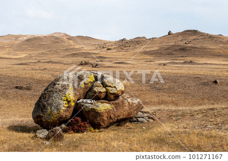 White bones lie between large boulders in the form of an altar in the steppe. Brown tones. Cloudy. The hills are behind. White bones lie between large boulders in the form of an altar in the steppe. Brown tones. Cloudy. The hills are behind. 101271167