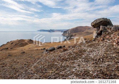 The shore of Lake Baikal with stones in the foreground. High rocky shore. There are clouds on the blue sky. The lake is calm. The shore of Lake Baikal with stones in the foreground. High rocky shore. There are clouds on the blue sky. The lake is calm. 101271168
