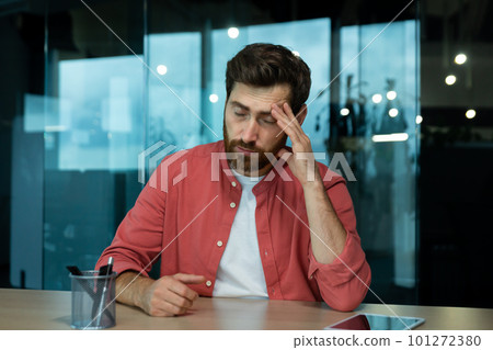Shocked and upset young man sitting at desk in office, thoughtfully holding head with hand, closed eyes, crying, feeling pain Fired from job, salary reduction, unemployed. 101272380