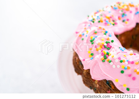 Funfettti bundt cake frosted with pink vanilla buttercream frosting and decorated with rainbow sprinkles. 101273112