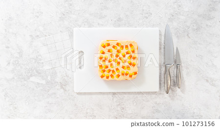 Flat lay. Scoring candy corn fudge using a parchment paper template for cutting into small pieces. Flat lay. Scoring candy corn fudge using a parchment paper template for cutting into small pieces. 101273156