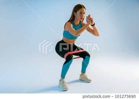 Athletic woman trains legs with fitness elastic band on studio background Athletic woman trains legs with fitness elastic band on studio background 101273690