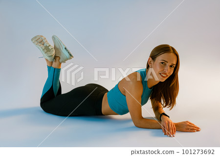 Attractive smiling woman wearing sportswear lying down on studio background Attractive smiling woman wearing sportswear lying down on studio background 101273692