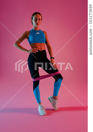 Athletic woman trains legs with fitness elastic band on studio background 101273694