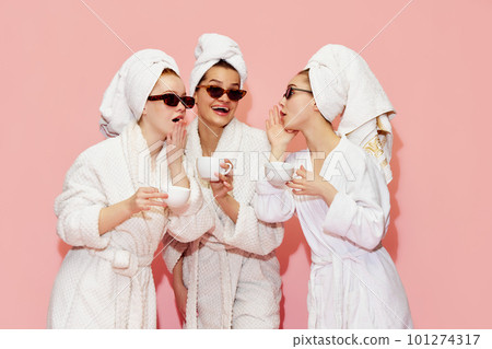 Spreading secrets. Three attractive girls in bathrobes and towels, drinking coffee and talking against pink studio background Spreading secrets. Three attractive girls in bathrobes and towels, drinking coffee and talking against pink studio background 101274317
