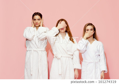 Three girls in bathrobes covering eyes, mouth and ears, posing against pink studio background. Keeping secrets 101274319