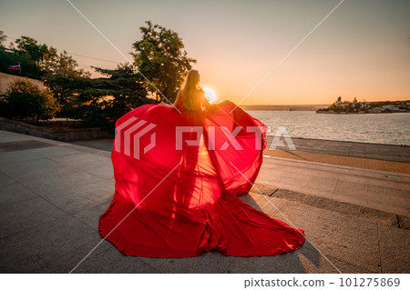 Sunrise red dress. A woman in a long red dress against the backdrop of sunrise, bright golden light of the sun's rays. The concept of femininity, harmony. 101275869
