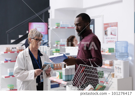 African american client discussing with pharmacist asking for help with cardiology drugs, worker explaining medical leaflet. Drugstore employee offering support assistance, medicine service 101276417