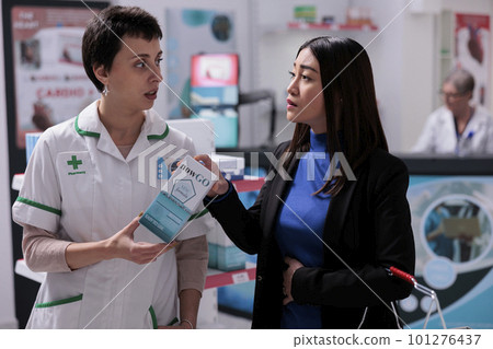 Young asian woman explaining gastritis symptoms to drugstore assistant and choosing stomachache medicaments. Pharmaceutical specialist recommending customer remedy from stomach pain 101276437