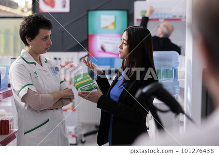 Young asian woman and drugstore chemist arguing about aspirin pills price in pharmacy retail store. Unsatisfied buyer complaining to pharmaceutical consultant in apotchecary 101276438