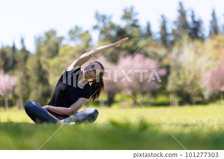 An adult woman sitting in lotus position and bending to the side 101277303