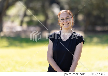 An adult smiling woman wearing glasses and sports clothes standing in the park - looking in the camera 101277312