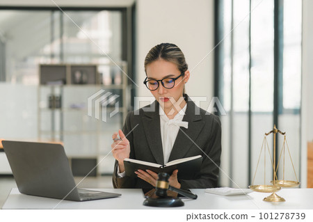 A businesswoman and lawyers are discussing contract papers with a brass scale on a desk in an office. The concepts of law, legal services, advice, justice, and real estate are being discussed. 101278739