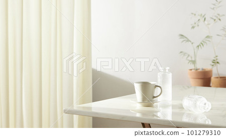 A room with a calm atmosphere, with clay pots placed in front of the wall and curtains letting in natural light. Glass bottles, coffee, and various objects on a marble table 101279310