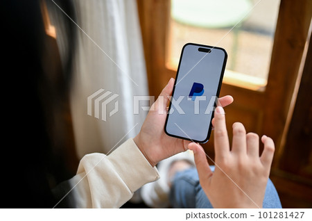A woman using PayPal on her iPhone. PayPal app logo on iPhone screen. 101281427