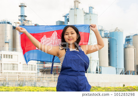 Positive girl in overalls with the Cambodia flag in her hands against the background of chimneys of modern factory 101283298