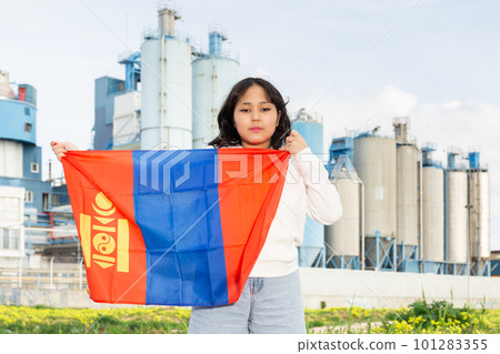 Sad young woman with flag of Mongolia against background of factory 101283355