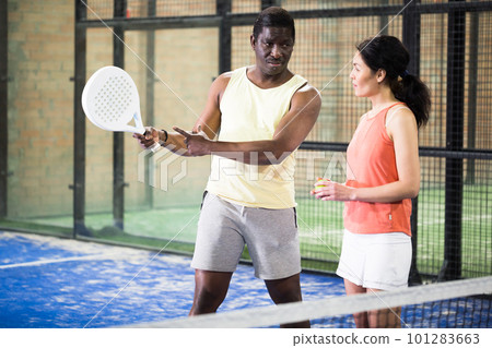 African american trainer teaches woman to play padel on tennis court African american trainer teaches woman to play padel on tennis court 101283663