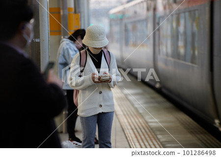 一位年輕女子在車站月台等火車時看著她的智能手機 一位年輕女子在車站月台等火車時看著她的智能手機 101286498