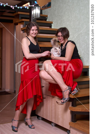 Two female dancers in red skirts and black tank tops are talking in a room next to the stairs and stroking a cat Two female dancers in red skirts and black tank tops are talking in a room next to the stairs and stroking a cat 101287680