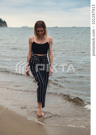 Young woman standing on blurred beachside background. Attractive female enjoying walking the sea shore. travel and active lifestyle concept. Springtime. Relaxation, youth, love, lifestyle solitude 101287913