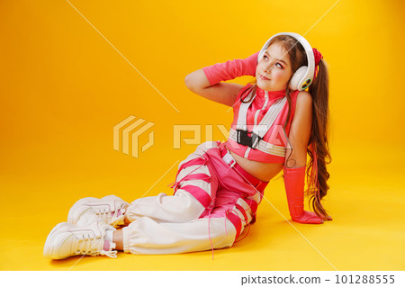 a teenage girl in a pink stage costume and headphones on a yellow background.  101288555