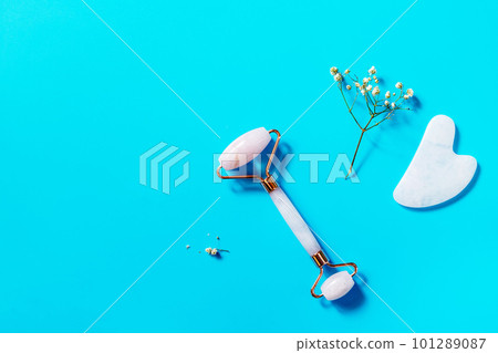 Rose quartz facial massage roller over blue background. Massage tools with jade stone, anti-wrinkle beauty skincare tool. View from above. Copy space. Rose quartz facial massage roller over blue background. Massage tools with jade stone, anti-wrinkle beauty skincare tool. View from above. Copy space. 101289087