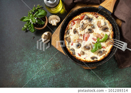 Frittata is an Italian breakfast dish. Omelette with mushrooms and bacon on a dark stone table. View from above. Copy space. 101289314