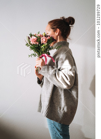 Woman in grey knitted sweater with bouqet of flowers in hands on white background Woman in grey knitted sweater with bouqet of flowers in hands on white background 101289729