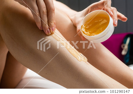A young slender girl applies sugar paste for hair depilation on her legs. 101290147