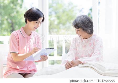 Home-visit nursing Caregiver interviewing a senior woman sitting on a bed 101290999