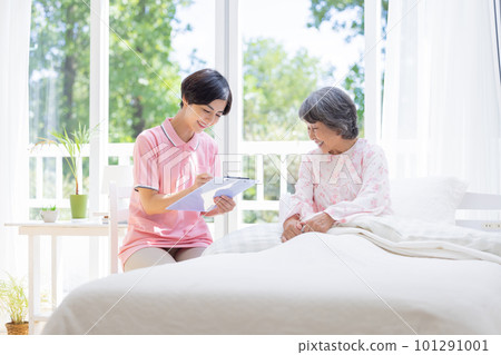 Home-visit nursing Caregiver interviewing a senior woman sitting on a bed 101291001