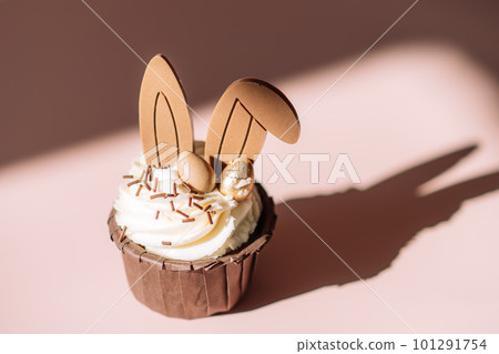 Easter cupcake with rabbit ears on pink background under hard light 101291754