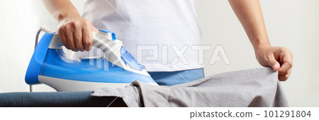 Woman at home electric ironing and pile clothes variety of colors. Woman ironing shirt on ironing board with steaming blue iron. housework and household concept. 101291804