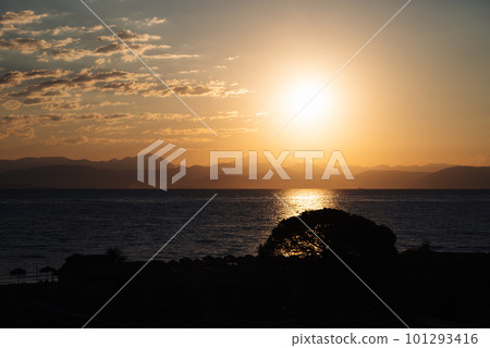 Sunrise From Corfu Island Overlooking Mountains Of Balkan Peninsula Of Greece, Moraitika, Corfu. In Foreground Are Silhouettes Of Trees And Water Slide. Sunrise From Corfu Island Overlooking Mountains Of Balkan Peninsula Of Greece, Moraitika, Corfu. In Foreground Are Silhouettes Of Trees And Water Slide. 101293416