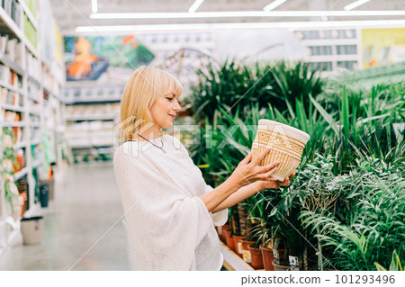 Gardening, planting and shopping concept. Beautiful mature adult woman choosing houseplants and pots in greenhouse or garden centre. Senior buying flowers plants at market store in mall Gardening, planting and shopping concept. Beautiful mature adult woman choosing houseplants and pots in greenhouse or garden centre. Senior buying flowers plants at market store in mall 101293496