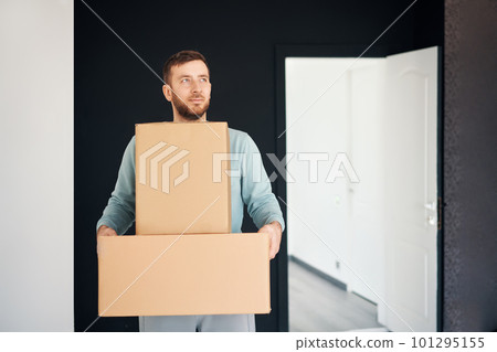Young smiling man moving into new apartment carrying cardboard boxes Young smiling man moving into new apartment carrying cardboard boxes 101295155
