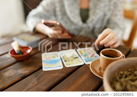 Fortune teller with tarot cards on table near burning candle.Tarot cards spread on table with magic herbs and palo santo aroma sticks. Forecasting concept Fortune teller with tarot cards on table near burning candle.Tarot cards spread on table with magic herbs and palo santo aroma sticks. Forecasting concept 101295601