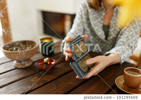Fortune teller with tarot cards on table near burning candle.Tarot cards spread on table with magic herbs and palo santo aroma sticks. Forecasting concept 101295608