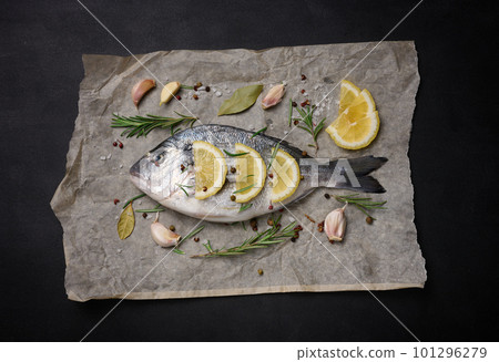 Raw whole dorado fish on brown parchment paper and spices for cooking, top view on black table 101296279
