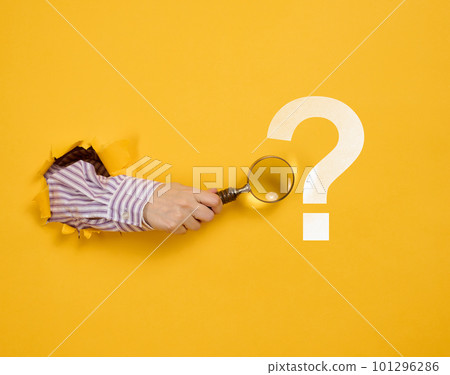 Female hand holds a magnifying glass on a yellow background, part of the body sticks out of a torn hole in a paper background. Business concept, finding information, answering questions Female hand holds a magnifying glass on a yellow background, part of the body sticks out of a torn hole in a paper background. Business concept, finding information, answering questions 101296286