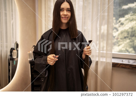 Smiling beautiful girl holds scissors and bun of her cut hair in her hands 101297372