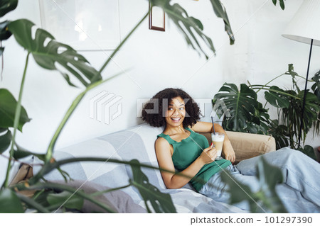Beautiful laughing african american in casual clothes sits on sofa with cup of latte in her hands. Beautiful laughing african american in casual clothes sits on sofa with cup of latte in her hands. 101297390