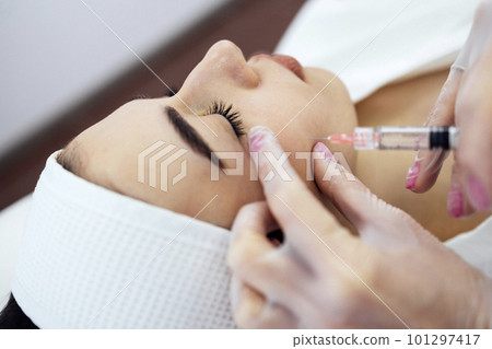 Female cosmetologist in transparent gloves makes an injection in the lower jaw of her client 101297417