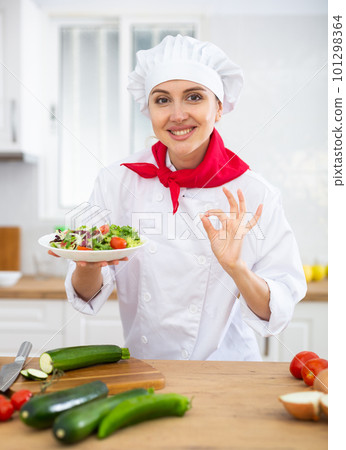Female chef in white uniform showing approving gesture satisfied with vegetable salad Female chef in white uniform showing approving gesture satisfied with vegetable salad 101298364
