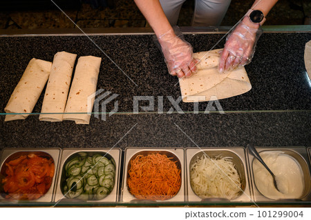 The cook in disposable gloves twists the shawarma on the work surface. The cook in disposable gloves twists the shawarma on the work surface. 101299004
